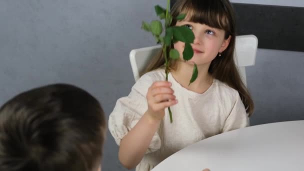 Um menino bonito dá a uma menina bonita de cabelos escuros flores, uma rosa vermelha. Presentes para o feriado, flores para o dia dos namorados. Movimento lento. — Vídeo de Stock