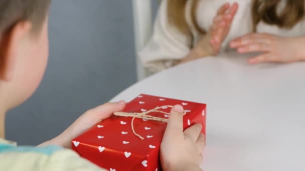 A little boy gives a beautiful red box with hearts as a gift for Valentines Day to his beloved girl. Valentines day celebration — Stock Video