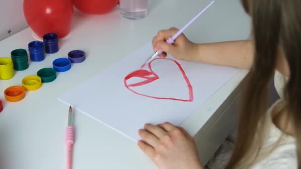 女の子はバレンタインデーの贈り物として赤い塗料で心をペイントします。愛のサインだ。子供への贈り物だ。絵の具で描く — ストック動画