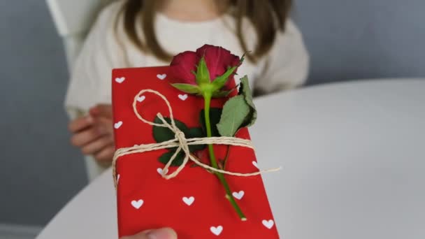 En söt pojke ger en mörkhårig söt flicka en presentask. Vacker röd låda med hjärtan. Långsamma rörelser. — Stockvideo