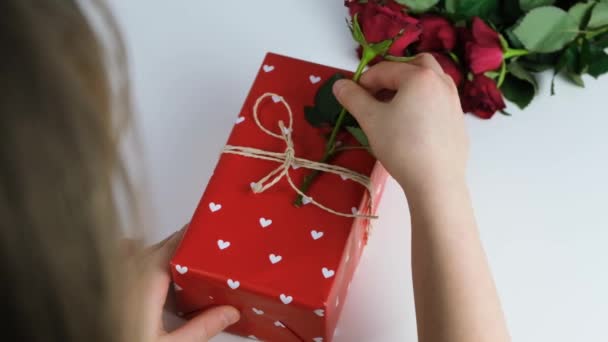 귀여운 소녀가 빨간 장미가 있는 아름다운 선물 상자를 장식 합니다. 축일 선물을 장식하고 포장하는 일. 느린 동작 — 비디오