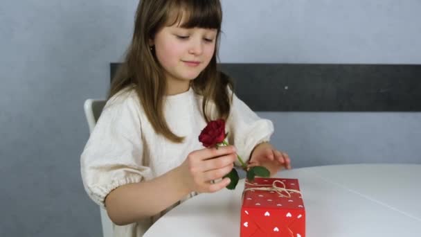 A cute girl decorates a beautiful gift box with a red rose. Decorating and wrapping gifts for the holidays. Slow motions — Stock Video