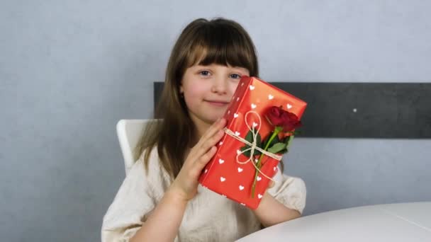 Cute little girl rejoices with a gift box decorated with a fresh red rose. Gifts for the holidays, decoration of gift wrapping — Stock Video