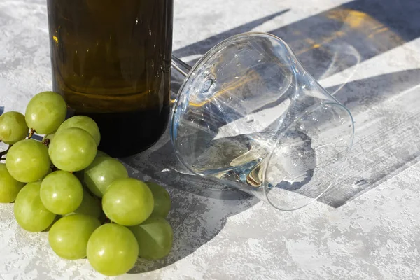 Bicchiere di vino accanto a un grappolo d'uva e una bottiglia al sole. Primo piano. Posto per il testo. Fondo grigio. — Foto Stock