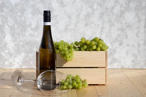 포도가 가득 담긴 나무 상자 옆에는 흰 포도주 한 병이 놓여 있다. 와인과 과일 음료의 생산. 써니 데이. 복사 공간 — 스톡 사진