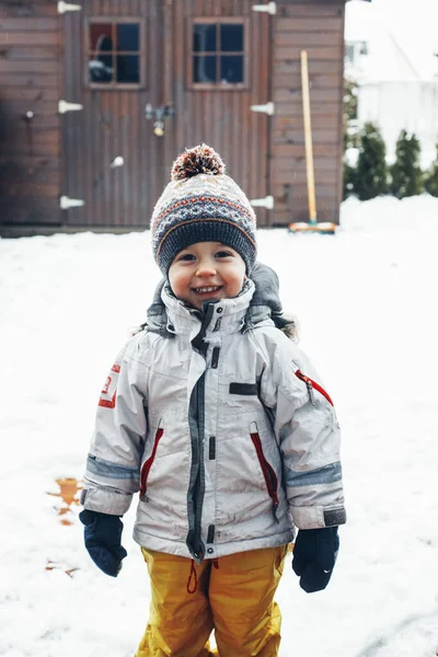 Ritratto di un simpatico ragazzo bambino contento in abiti invernali all'aperto nella neve. Tempo invernale, divertimento invernale, infanzia felice. Orientamento verticale — Foto Stock