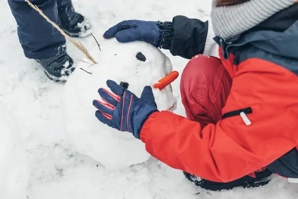 Il primo piano di una ragazza fa la faccia a un pupazzo di neve. Giochi invernali all'aperto. — Foto Stock
