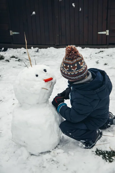 Giochi all'aperto in inverno. Bambino carino ragazzo caucasico di sei anni nella neve scolpisce un pupazzo di neve. Giochi invernali, periodo invernale — Foto Stock