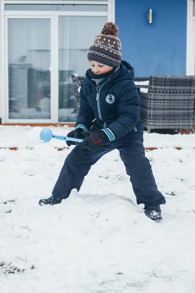 Carino ragazzo caucasico sta giocando palle di neve nel cortile della casa. Divertimento invernale e giochi, vacanze e riposo. — Foto Stock