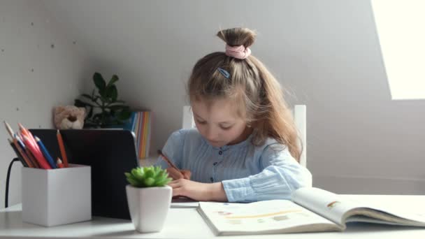 Otthoni tanulás, otthoni iskola online. Kaukázusi aranyos kislány csinál házi feladatot egy tablettát, és nagyon fáradt. Videofelvétel 4K. Tanulás otthon és a karantén ideje alatt — Stock videók