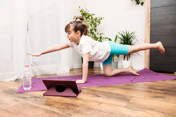 Evde yoga, esneme ya da jimnastik yapan beyaz bir kız. Çevrimiçi çocuklar için spor, sağlıklı yaşam tarzı.