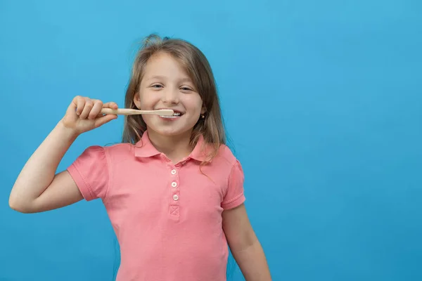 Concept dentaire. Gros plan portrait d'une jolie fille qui se brosse les dents avec un pinceau écologique sur fond bleu. Soins buccodentaires, prévention des caries. — Photo