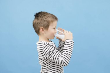 Beyaz tatlı çocuk mavi arka plandaki cam bardaktan süt ya da kefir içiyor. Çocuklar için süt ve mayalanmış süt ürünlerinin faydaları. Boşluğu kopyala