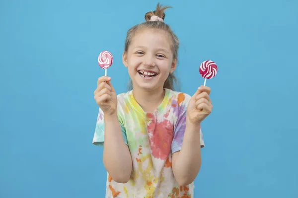 Le concept de vacances, divertissement amusant et la joie des enfants. Une jolie fille aux cheveux bruns dans un T-shirt multicolore tient des sucettes rondes et sourit. — Photo