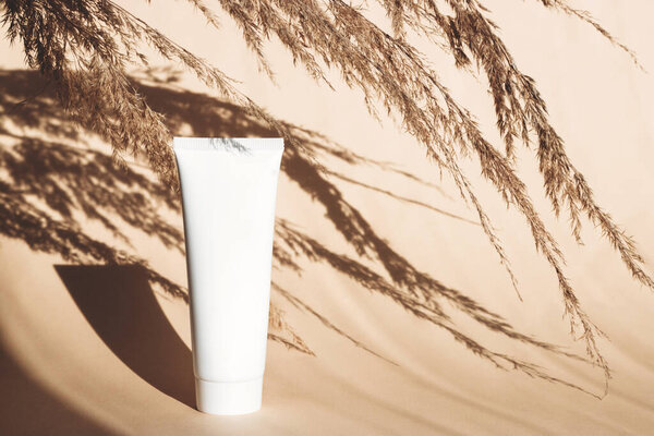 Белая пустая трубка на бежевом фоне с твёрдыми тенями. Чистый наклейка, готовый макет для рекламы. Место для смс. Летние средства для ухода за кожей