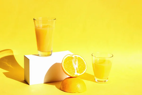 Jugo de naranja fresco y jugoso en vasos en pasarelas blancas de moda con sombras duras sobre un fondo amarillo. Concepto de comida y bebida saludable. Copiar espacio —  Fotos de Stock
