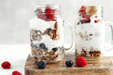 Sağlıklı gıda konsepti. Kahvaltı ya da atıştırmalık. Yoğurtlu granola, taze ahududu ve cam kavanozlarda yabanmersini..