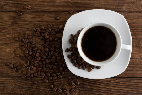 White cup of black freshly brewed coffee on a wooden table and grains are scattered nearby. Morning espresso, breakfast in a cafe or restaurant. Stock Image