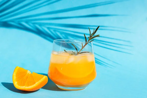 Bebida refrescante, cóctel, limonada o zumo de naranja con rodajas de fruta fresca sobre un fondo azul con una sombra de una hoja de palma. Copiar espacio —  Fotos de Stock