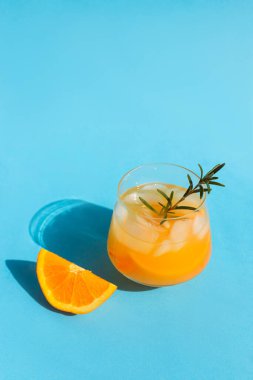 Limonata, portakal kokteyli, buzlu ferahlatıcı yaz içeceği mavi arka planda biberiye filizi. Dikey fotoğraf. Boşluğu kopyala