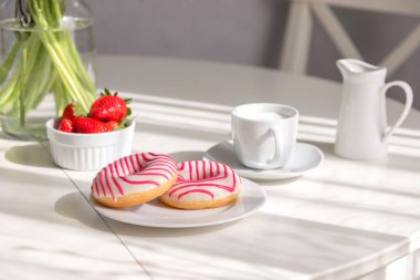 Mutfakta bir buket çiçek, çörek, kahve ve taze çilekle romantik bir kahvaltı. Güneşli bir günde kahvaltı.