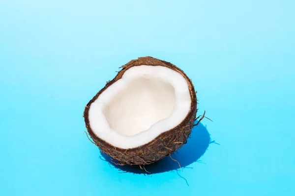 Minimalism concept. A creative layout of half a coconut in the bright summer sun with shadows on a blue background. — Fotografia de Stock