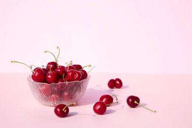 Pembe ve beyaz arka planda taze ve sulu kirazlarla dolu bir cam kase. Mesajın için yer aç. Mevsimlik yaz meyveleri ve meyveleri