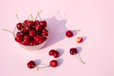 Cam bir kasede pembe pastel arka planda taze, sulu kirazlar. Mevsimlik böğürtlen ve meyve. Metin için yer