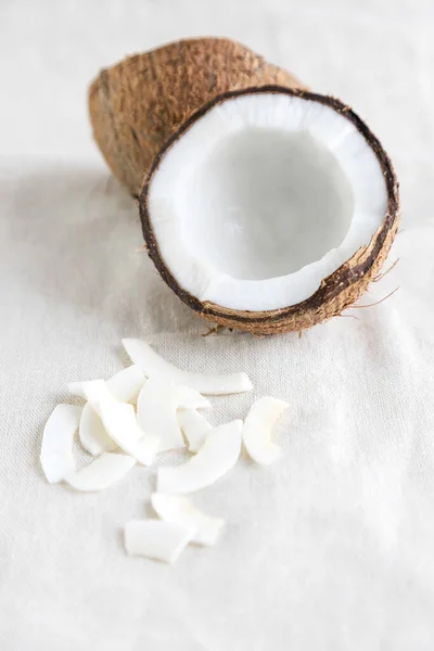 Kokosnusssplitter auf einer Tischdecke aus Leinen und eine halbe frische Kokosnuss in der Nähe. Ein gesunder Snack ideal für Ernährungswissenschaftler, Veganer und Vegetarier. — Stockfoto