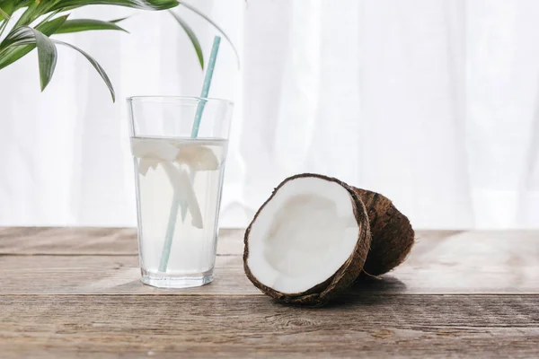 Νερό καρύδας σε ποτήρι πάνω σε ξύλινο τραπέζι με ανοιχτή καρύδα με λευκό πολτό. Ένα βιολογικό υγιεινό προϊόν διατροφής ιδανικό για χορτοφάγους και vegans. — Φωτογραφία Αρχείου