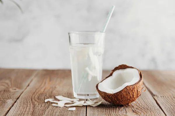 Ein Glas frisches Bio-Kokoswasser, Milch auf einem Holztisch und eine reife Kokosnusshälfte in der Nähe. Erfrischende vegetarische Getränke — Stockfoto