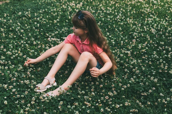 Roztomilá rozkošná dívka sedí na jetelové louce a sbírá kytici. Odpočinek a odpočinek v přírodě. Letní dovolená mimo město — Stock fotografie