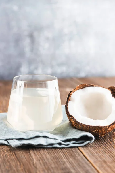 Ein Glas frisches Bio-Kokoswasser, Milch auf einem Holztisch und eine halbe saftige Kokosnuss daneben. Vertikales Foto. Kopierraum — Stockfoto