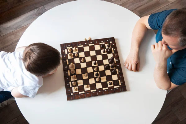 View from above Dad and son are playing a board game of chess. Time and games with children. Logic and strategy game. Authentic moments from real life