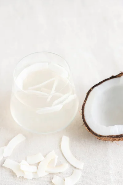 Água de coco ou leite em um copo, batatas fritas de coco e metade de um coco fresco e suculento estão ao lado dele. Lanche vegetariano, lanche saudável. Foto vertical — Fotografia de Stock