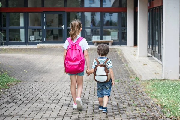 A girl and a boy, brother and sister go by the hand to school, educational institution, kindergarten. The beginning of lessons, classes after the holidays. Back to school — Stock Photo, Image
