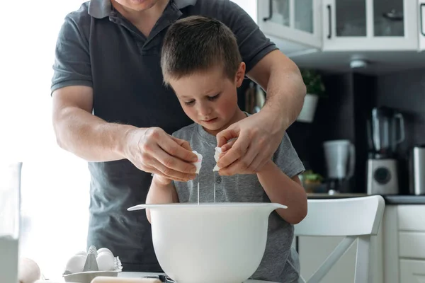 Dad and son are preparing cookies in the kitchen. Family traditions, fatherhood and activities with children. Authentic, real life moments