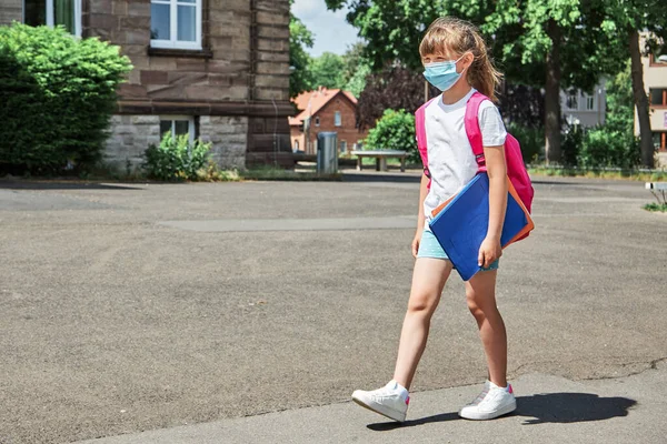 The girl goes to school with a backpack and a protective medical mask. Start of the school year, back to school. New reality amid a virus