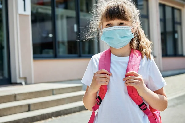 Okul bahçesinde maskeli bir kızın portresi. Virüsler ve grip salgınları sırasında çocukların ve okul çocuklarının korunması