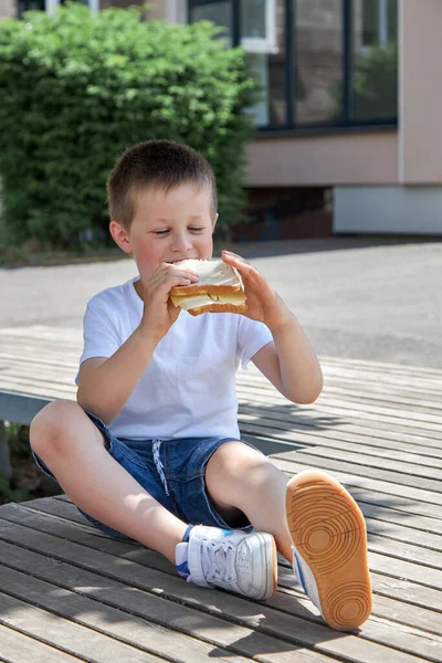 Aliments sains pour les enfants à l'école. Le garçon mange un sandwich fait maison, un déjeuner ou une collation dans la cour de l'école pendant les vacances. — Photo