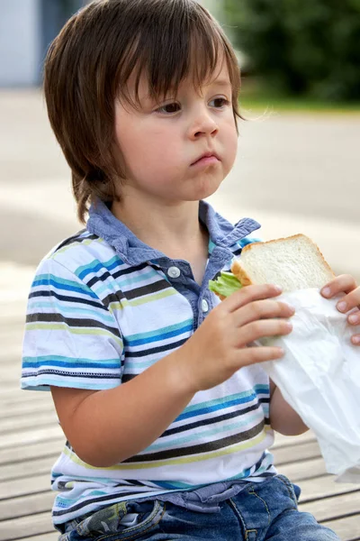 Школьники, дошкольник, мальчик обедает, перекусывает, завтракает во дворе школы. Еда для детей в учебных заведениях, детских садах. Здоровое питание. — стоковое фото