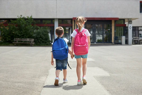 De volta à escola. Rapaz e rapariga vão para a escola com mochilas. O início do ano letivo, as crianças vão às aulas — Fotografia de Stock