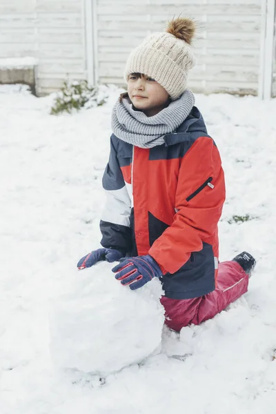 Una ragazza caucasica carina di 9 anni fa rotolare un pupazzo di neve nel cortile di casa. Neve divertimento e giochi, vacanze invernali. Stile di vita. — Foto Stock