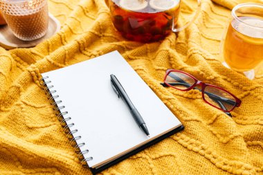 Boş günlük, kalem ve okuma bardakları çay eşliğinde rahat sarı bir battaniyede dinleniyor.