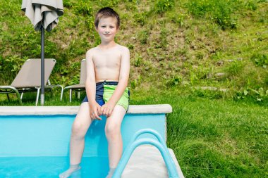 Genç çocuk havuzun kenarında dinleniyor, ayaklarını ferahlatıcı suya daldırıyor.