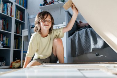 Mutlu çocuk yatak odasındaki karton kutudan oyun evi yaratıyor.