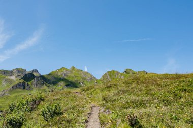 Mavi gökyüzünün altında görkemli yeşil dağlara doğru yükselen yürüyüş yolunun manzarası doğaya barışçıl bir kaçış sunuyor.