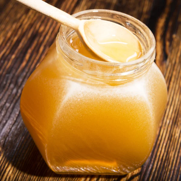 Jar of honey and spoon on a wooden background — Stock Photo, Image