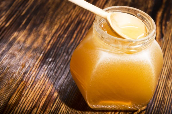 Jarra de mel e colher em um fundo de madeira — Fotografia de Stock
