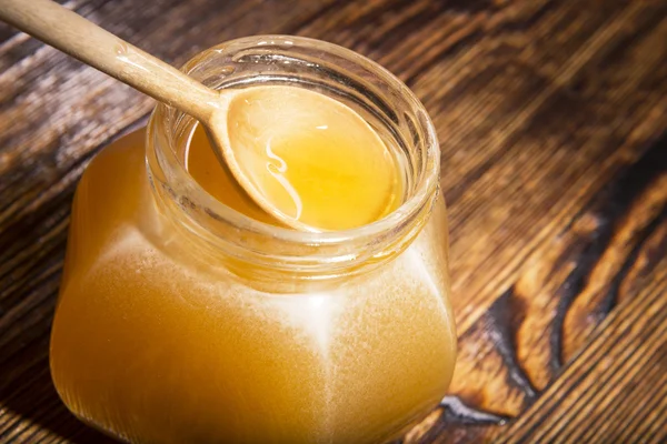 Jar of honey and spoon on a wooden background — Stock Photo, Image